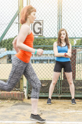 Runner passing young woman standing beside sports ground, London, UK - CUF30880