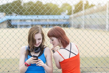 Junge Frauen benutzen ein Smartphone neben einem Zaun, London, UK - CUF30881