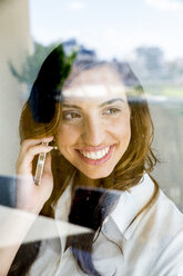 Young woman using smartphone, smiling, photographed through glass - CUF31110