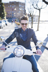 Portrait of smiling young man sitting on moped at roadside - CUF31113