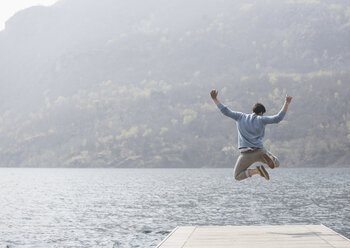 Rear view of young man jumping on pier, Lake Mergozzo, Verbania, Piemonte, Italy - CUF31127
