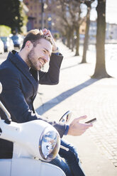 Stylish young man sitting on moped with smartphone - CUF31141