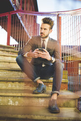 Stilvoller junger Mann mit Smartphone auf der Treppe einer Fußgängerbrücke sitzend - CUF31145