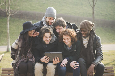 Sechs junge erwachsene Freunde benutzen ein digitales Tablet auf einer Parkbank - CUF31154