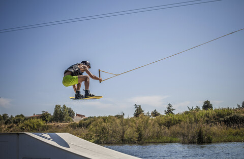 Mittlerer Erwachsener, männlicher Wakeboarder, der über eine Rampe im Meer springt, Cagliari, Sardinien, Italien, lizenzfreies Stockfoto