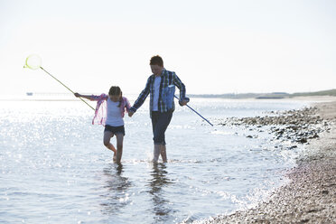 Mädchen und Junge paddeln im Wasser, halten sich an den Händen, tragen Fischernetze und schauen nach unten - CUF31207
