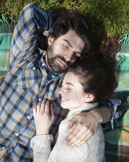 Blick von oben auf ein junges Paar, das mit geschlossenen Augen auf einer Picknickdecke liegt - CUF31284