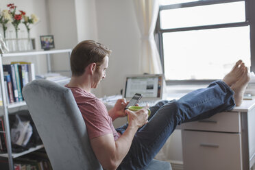 Mid adult man with feet up on desk reading smartphone texts - ISF09650