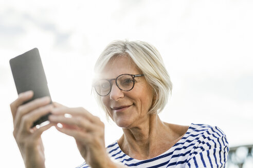 Lächelnde ältere Frau, die im Freien ein Mobiltelefon benutzt - FMKF05145
