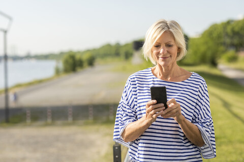 Lächelnde ältere Frau, die am Flussufer ein Mobiltelefon benutzt, lizenzfreies Stockfoto