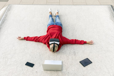 Senior woman lying on the ground wearing VR glasses next to mobile devices - FMKF05157