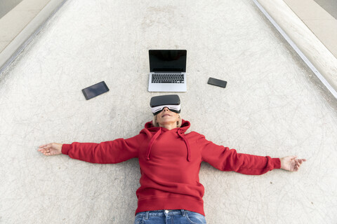 Senior woman lying on the ground wearing VR glasses next to mobile devices stock photo