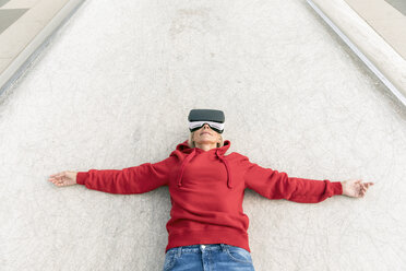 Senior woman lying on the ground wearing VR glasses - FMKF05159