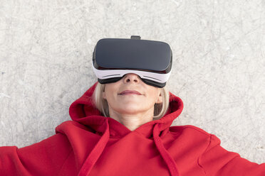 Senior woman lying on the ground wearing VR glasses - FMKF05160