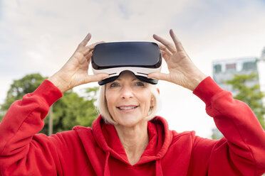 Portrait of smiling senior woman wearing VR glasses - FMKF05162