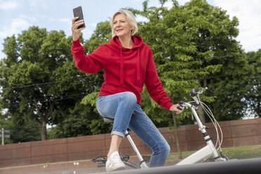 Senior woman with city bike using cell phone - FMKF05163