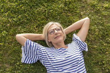 Portrait of smiling senior woman lying in grass - FMKF05170