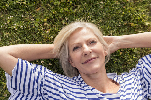 Porträt einer lächelnden älteren Frau, die im Gras liegt, lizenzfreies Stockfoto