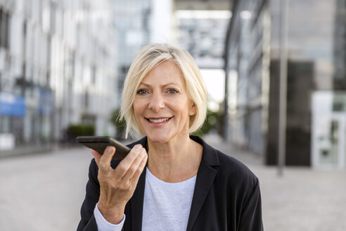 Porträt einer lächelnden älteren Geschäftsfrau, die ein Mobiltelefon im Freien benutzt - FMKF05188