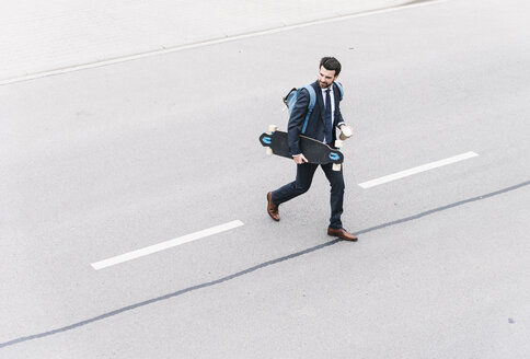 Businessman with takeaway coffee and skateboard walking on the street - UUF14081
