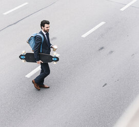 Businessman with takeaway coffee and skateboard walking on the street - UUF14082