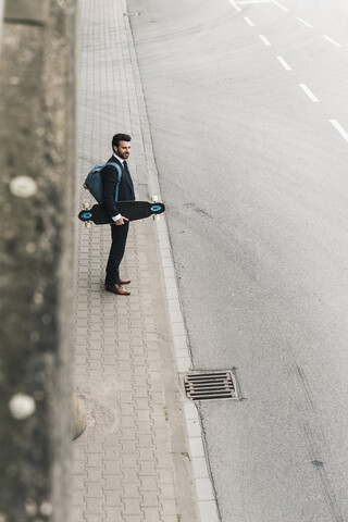 Geschäftsmann mit Skateboard an der Straße stehend, lizenzfreies Stockfoto