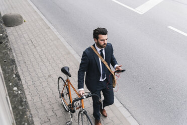 Geschäftsmann mit Fahrrad und Mobiltelefon zu Fuß auf der Straße - UUF14093