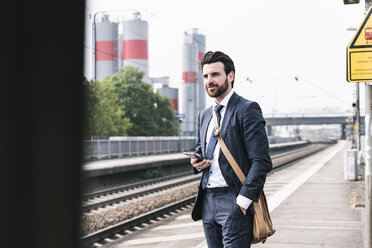 Businessman with cell phone waiting at the platform - UUF14101