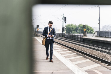 Geschäftsmann mit Mobiltelefon auf dem Bahnsteig - UUF14105