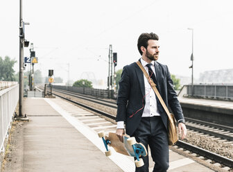 Geschäftsmann mit Skateboard und Kopfhörern auf dem Bahnsteig - UUF14107