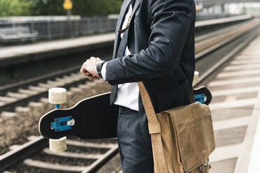 Nahaufnahme eines Geschäftsmannes mit Skateboard, der am Bahnsteig wartet - UUF14109