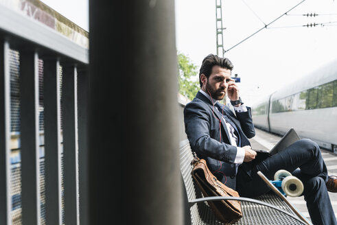 Geschäftsmann mit Skateboard, Laptop und Kopfhörern am Bahnsteig - UUF14112