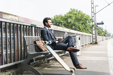 Smiling businessman with skateboard using laptop at the platform - UUF14113