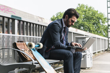 Businessman with skateboard using laptop at the platform - UUF14115