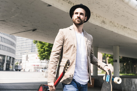 Young man with guitar and skateboard walking in the city stock photo