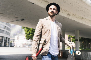 Junger Mann mit Gitarre und Skateboard zu Fuß in der Stadt - UUF14123