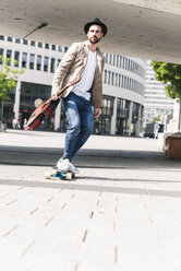Junger Mann mit Gitarre fährt Skateboard in der Stadt - UUF14124