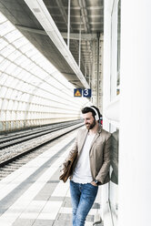 Junger Mann mit Kopfhörern, der am Bahnsteig wartet - UUF14129