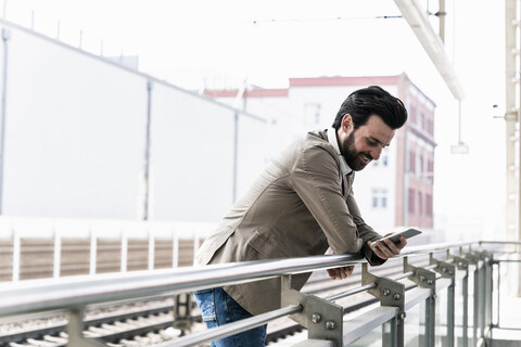 Lächelnder junger Mann mit Mobiltelefon auf dem Bahnsteig, lizenzfreies Stockfoto