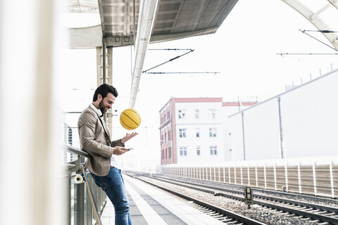 Smiling young man with cell phone and basketball at the station platform stock photo