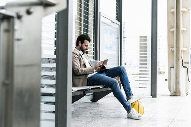 Young man with basketball using tablet at the station platform - UUF14138