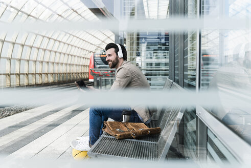 Junger Mann mit Basketball und Kopfhörern, der auf dem Bahnsteig ein Tablet benutzt - UUF14139