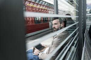 Junger Mann mit Tablet wartet auf dem Bahnsteig - UUF14141