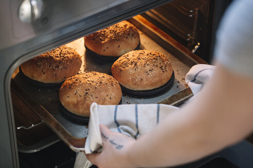 Frau nimmt selbstgemachte vegane Burgerbrötchen aus dem Ofen - ALBF00385