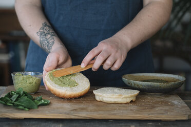 Frau bereitet veganen Burger zu, bestreicht Brötchen mit Avocadocreme - ALBF00392