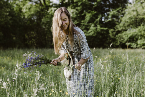 Italy, Veneto, Young woman plucking flowers and herbs in field - ALBF00414