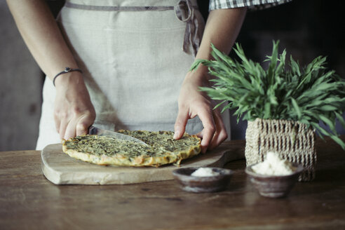 Junge Frau beim Schneiden von hausgemachtem Kichererbsen-Kräuter-Kuchen - ALBF00424