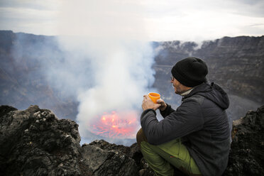 Afrika, Demokratische Republik Kongo, Virunga-Nationalpark, Mann sitzt über dem Nyiragongo-Vulkankrater - REAF00301