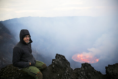 Afrika, Demokratische Republik Kongo, Virunga-Nationalpark, Mann sitzt über dem Nyiragongo-Vulkankrater, lizenzfreies Stockfoto