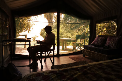 Uganda, Silhouette of a man reading in tent camp - REAF00311